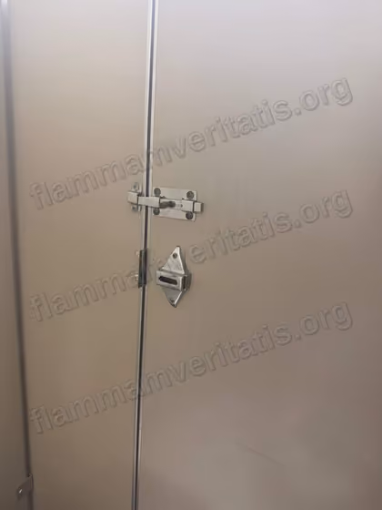 Puerta de un cubículo de baño con un pasador de barra atornillado arriba y, abajo, la placa del seguro original sin su pasador.