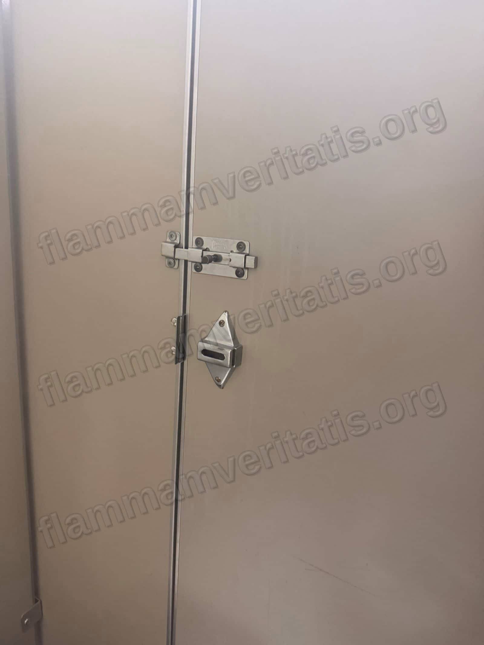 Puerta de un cubículo de baño con un pasador de barra atornillado arriba y, abajo, la placa del seguro original sin su pasador.