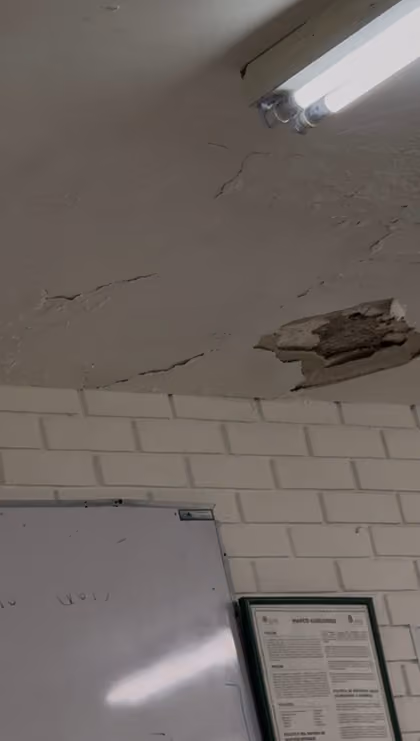 Techo del aula 3301 con una grieta grande y un trozo de aplanado desprendido junto a una lámpara, sobre un pizarrón y un cartel de la Facultad.