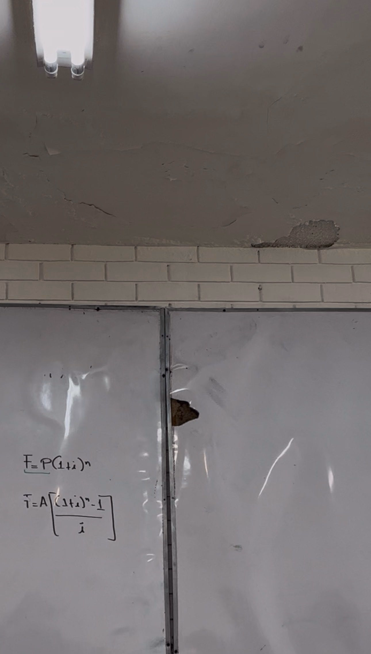 Techo del aula 3301 con grietas y un trozo de aplanado caído sobre el borde de ladrillo, encima de un pizarrón con una zona inflada y perforada.
