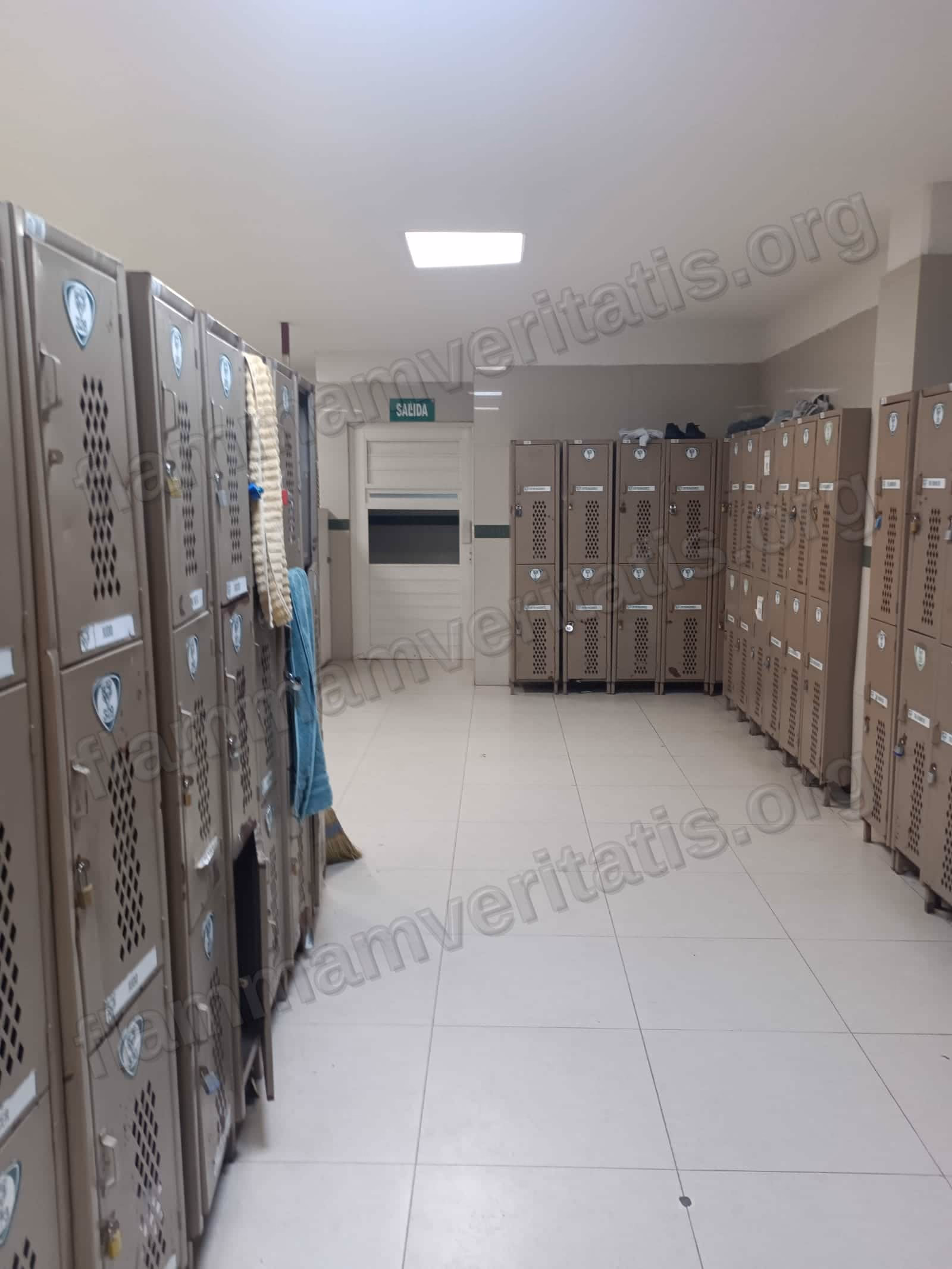Pasillo de vestidores del Polideportivo con filas de casilleros a ambos lados y una puerta de salida al fondo con letrero SALIDA.